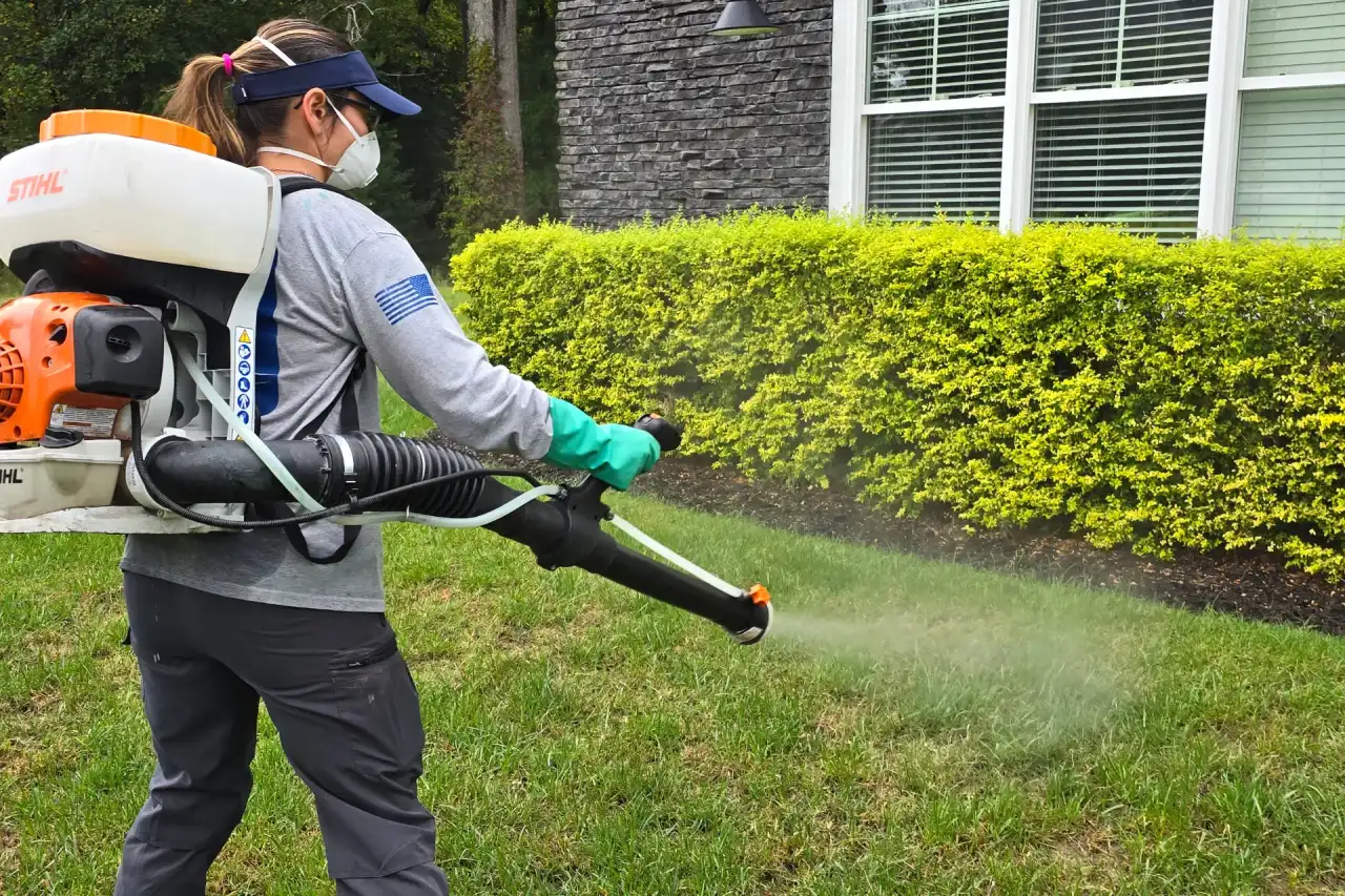 Meadow Lawn & Pest technician applying a barrier spray treatment along a wooded yard edge in Hampton Roads, Virginia