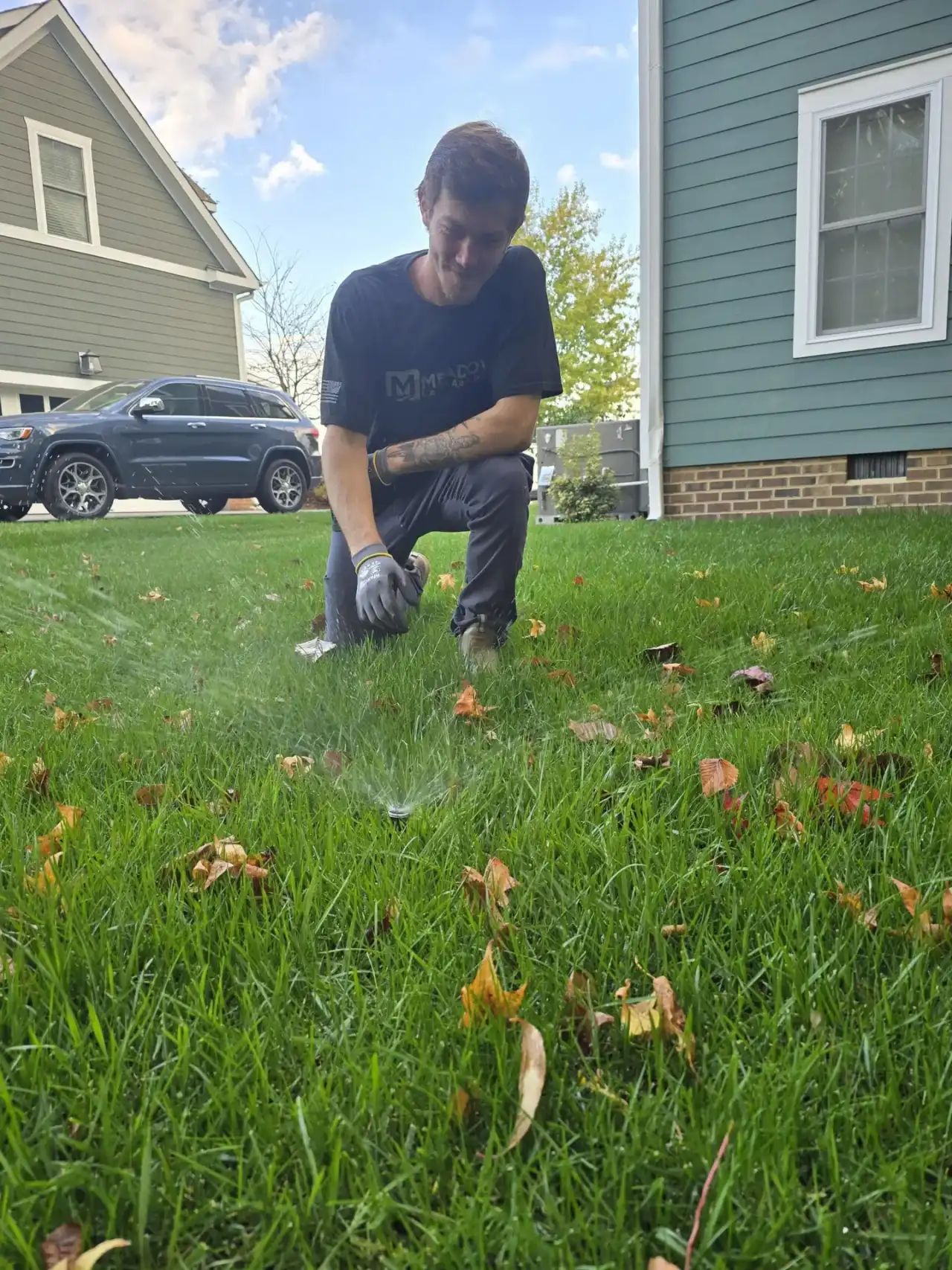 Technician kneeling to check a spraying sprinkler head in a green residential lawn