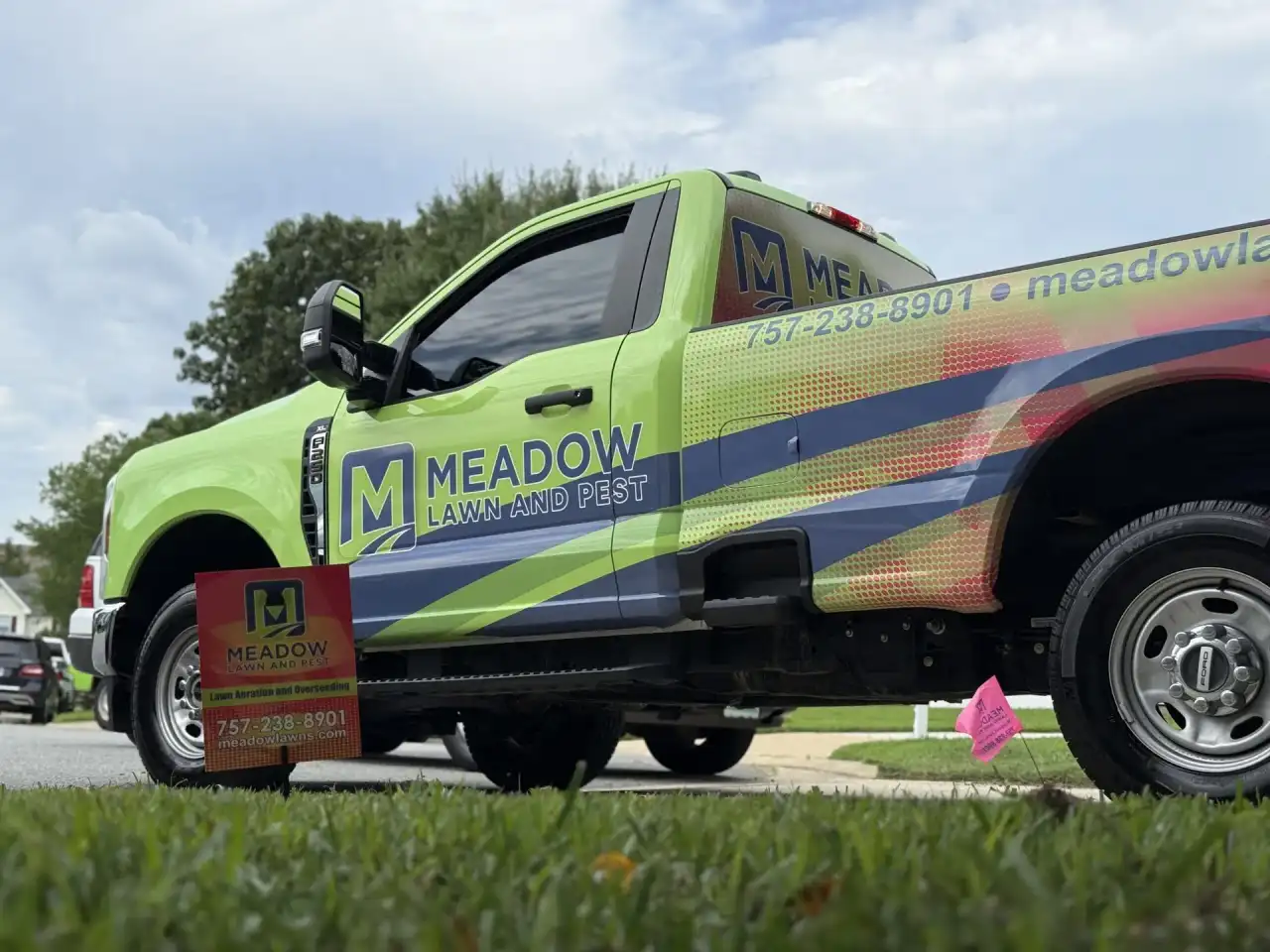 Meadow Lawn and Pest wrapped Ford truck parked at a Carrollton home with lawn service yard sign
