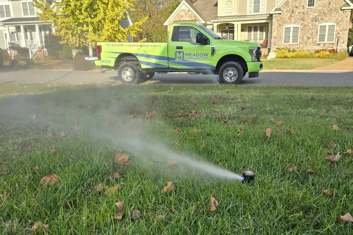 A Meadow Lawn and Pest truck at a home with a sprinkler running before winterization